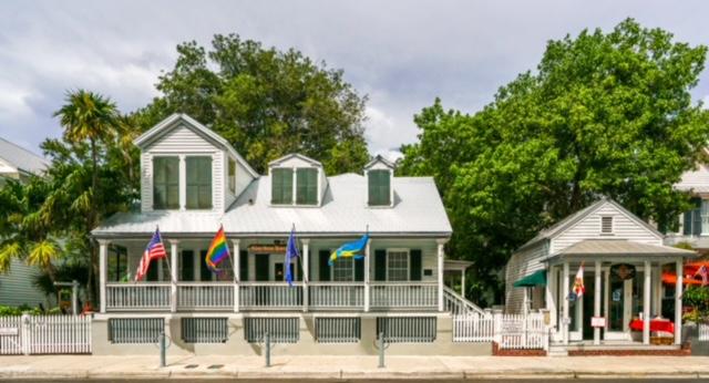 Two houses with flags in front, surrounded by trees and a white fence.