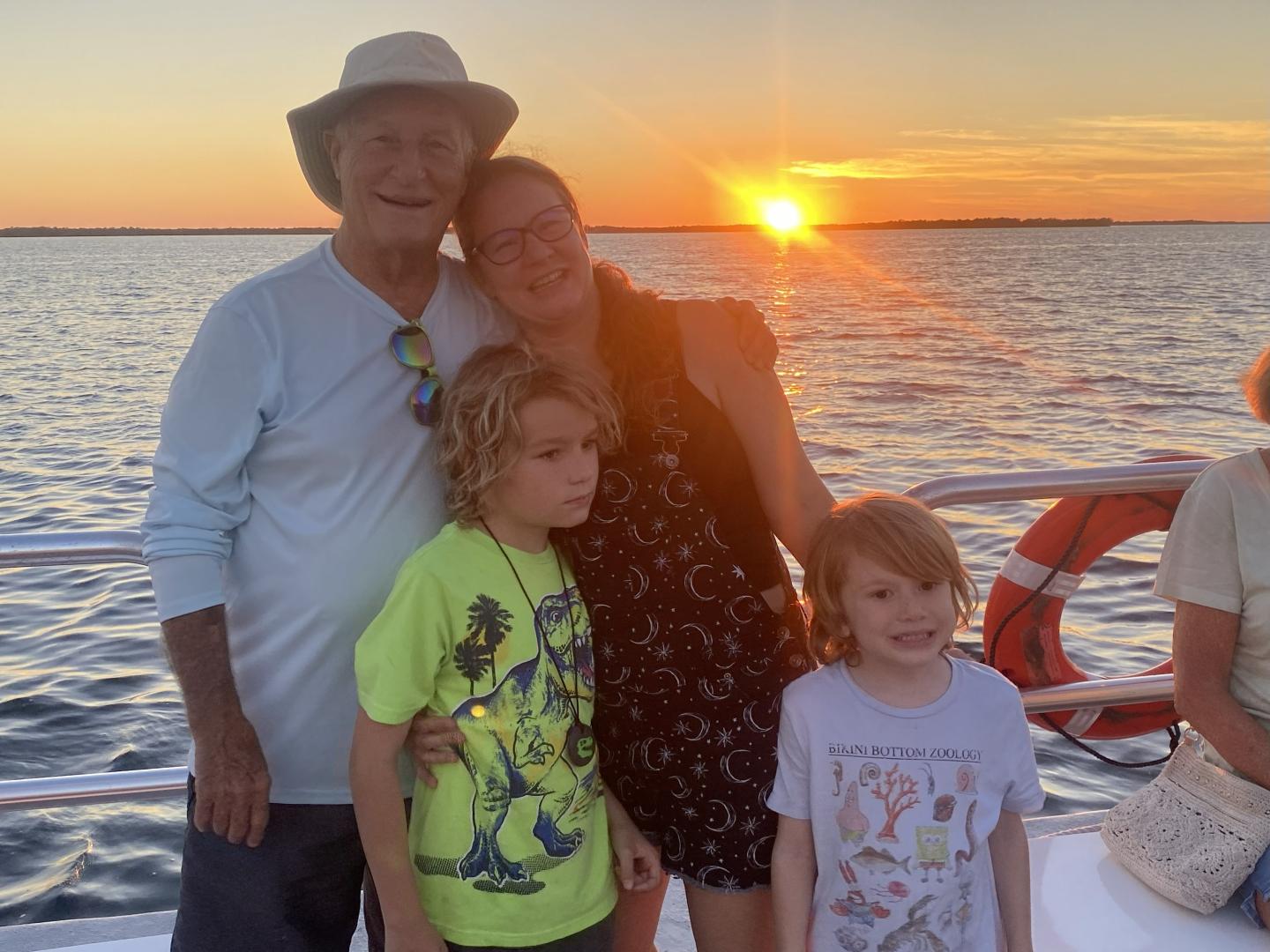 Family on a boat at sunset, smiling with ocean in the background.