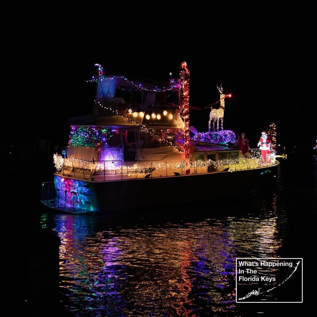 Festive boat with colorful lights and a reindeer decoration on top, reflecting on water.