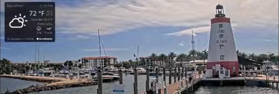 Lighthouse by a marina on a sunny day with few clouds.