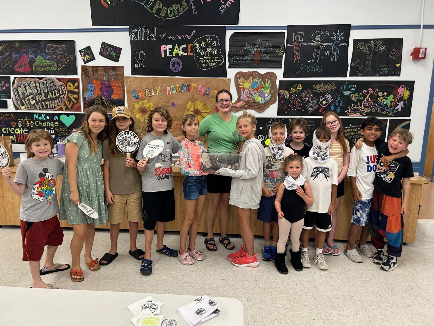 Children and adults in a classroom holding artwork, smiling. Colorful art decorates the walls.