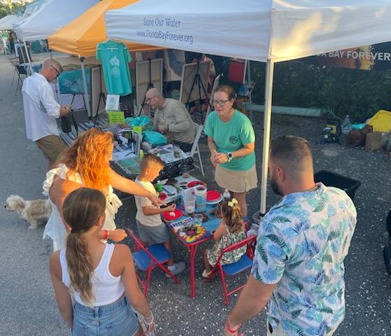 People gathered at a colorful outdoor market booth, children seated at a small table.