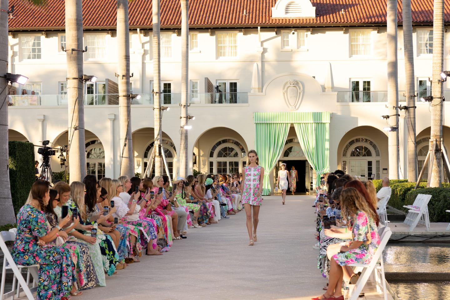 Lilly Pulitzer outdoor fashion show in Key West with model walking on runway, audience seated on both sides.