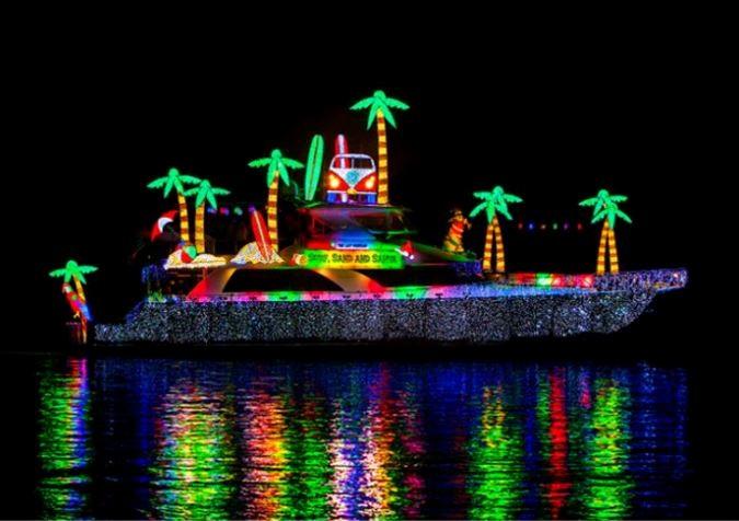 Festive boat decorated with neon palm trees and lights, reflects on water at night.