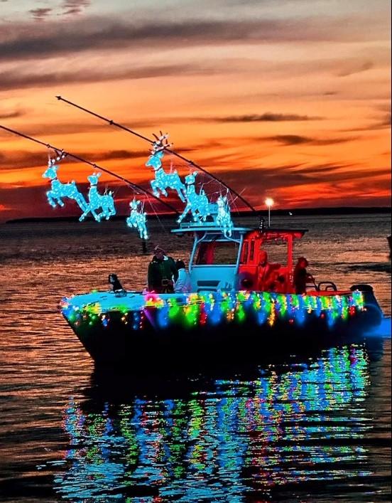 Boat with Christmas lights and reindeer decorations, sunset in the background.