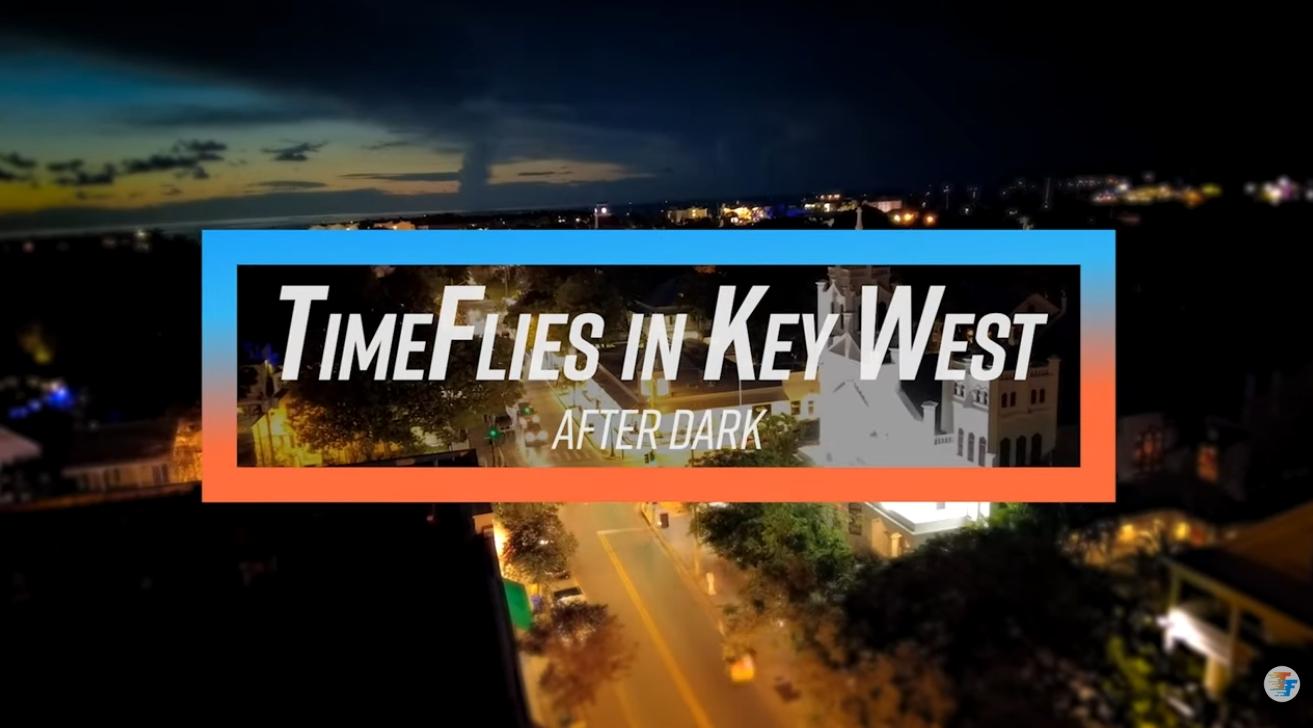 Night aerial view of a city street, trees, and dark blue sky.