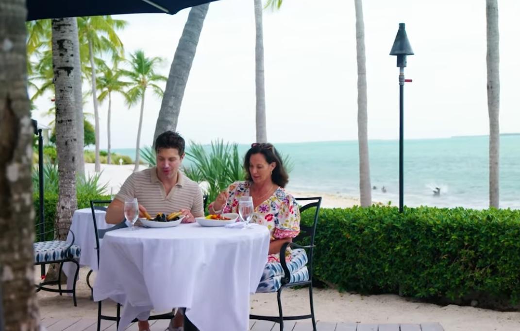Couple dining outdoors by the beach under palm trees.