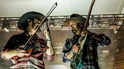 Two musicians in cowboy hats playing violin and guitar on stage.