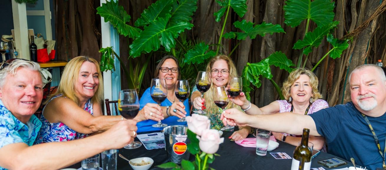 Friends toasting with wine glasses around a table, smiling.