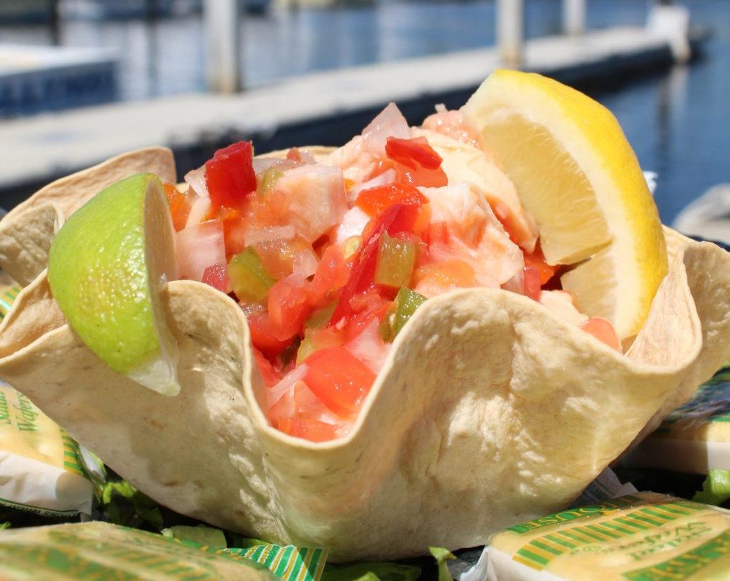 Shrimp cocktail in a tortilla bowl with lime and lemon wedges.