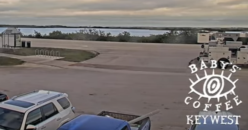 Parking lot near water under cloudy sky, logo at bottom right.