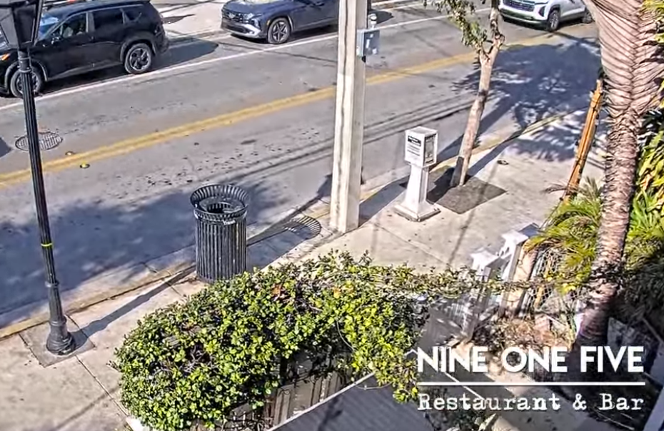 Restaurant patio with street view, cars, and greenery.