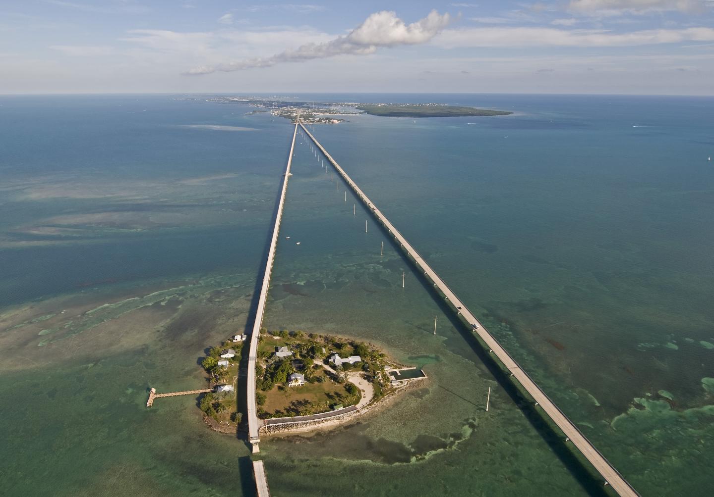 Aerial view of a long bridge stretching over a blue sea with an island below.