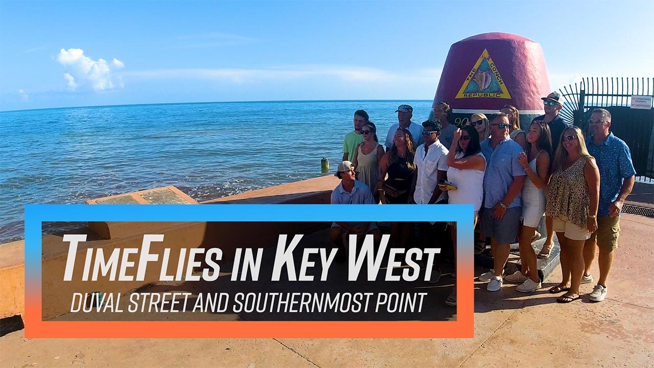A group of people pose by a large buoy at the ocean's edge under clear skies.