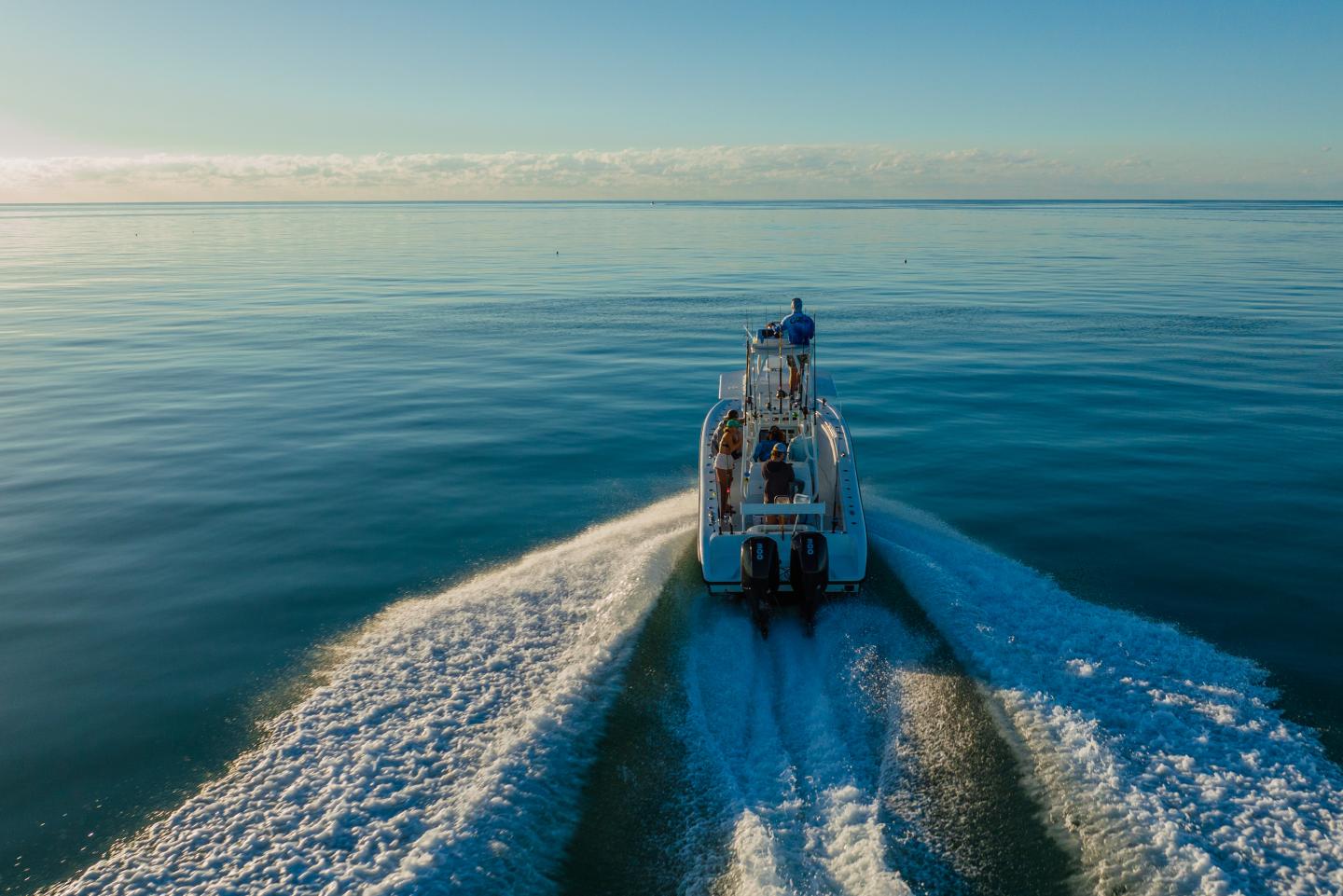 A boat speeding on calm blue water under a clear sky.