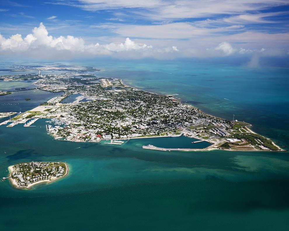 Aerial view of a coastal city surrounded by turquoise ocean and clear sky.