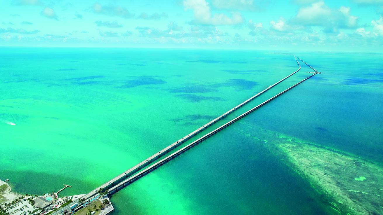 Aerial view of a long bridge over turquoise ocean.