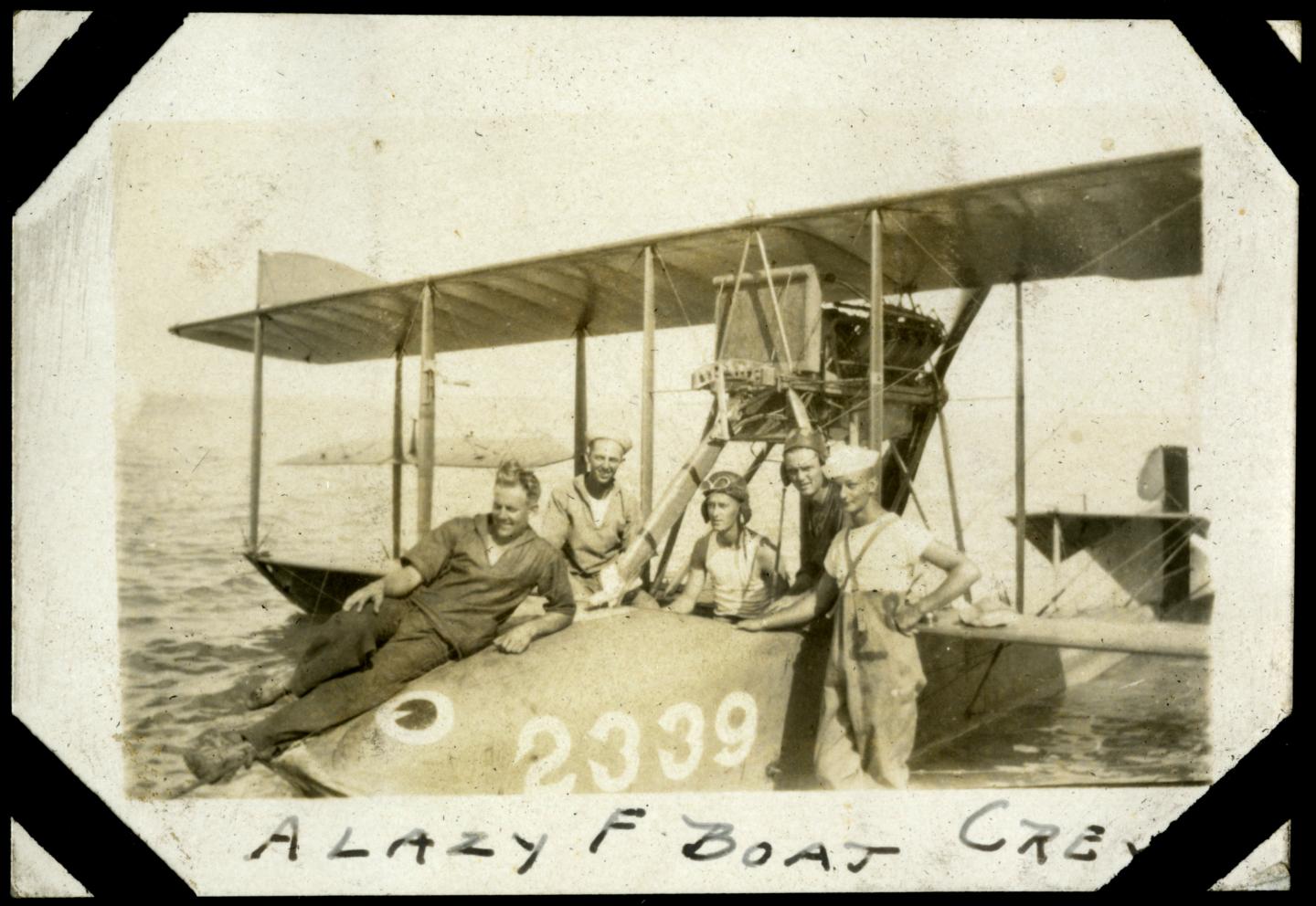Aeroplane on water with three men posing, one seated on the wing. Vintage sepia photograph.