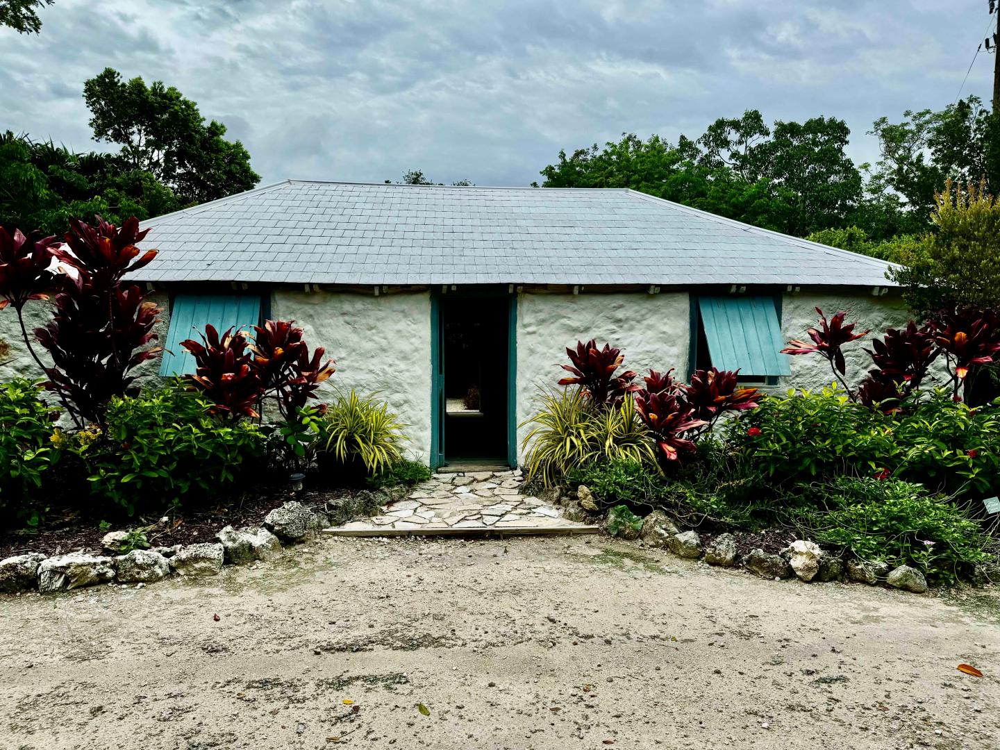 Small white house with a tin roof, surrounded by lush plants. 