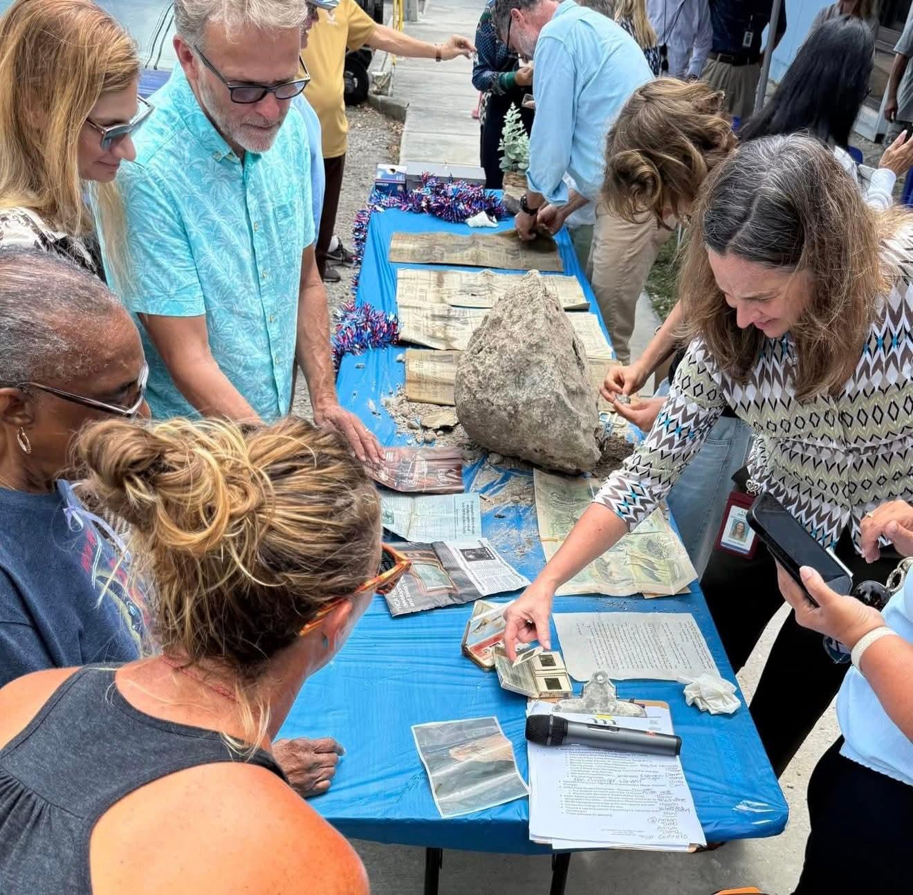 People examining artifacts on a blue table outdoors.