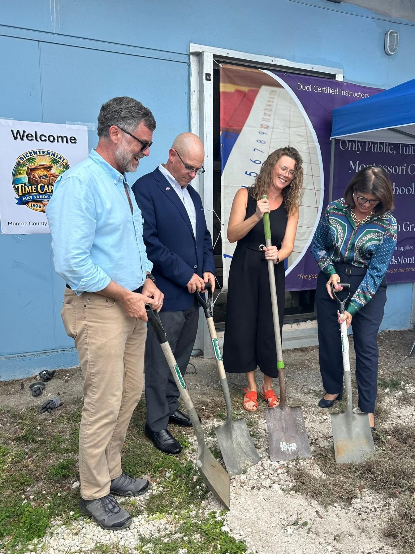 Four people with shovels breaking ground at an outdoor event.