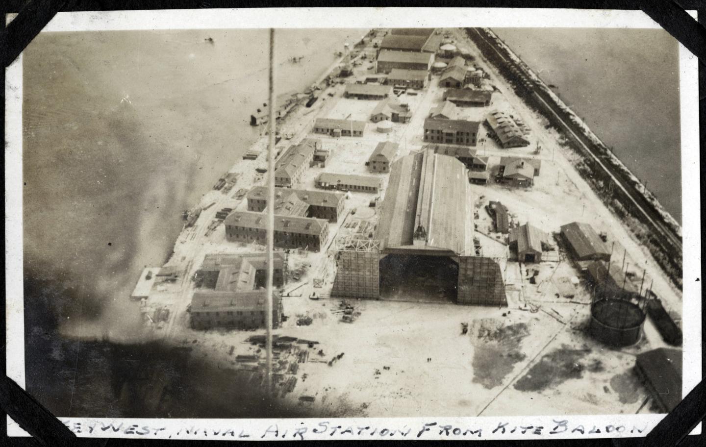 Aerial view of a shipyard with buildings and a large structure, bordered by a river.