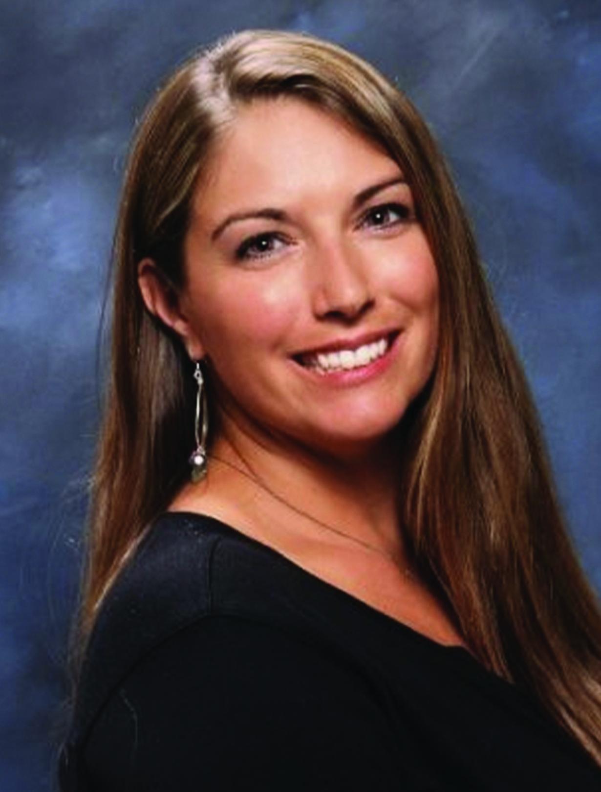 Smiling woman with long brown hair on a blue-gray background.
