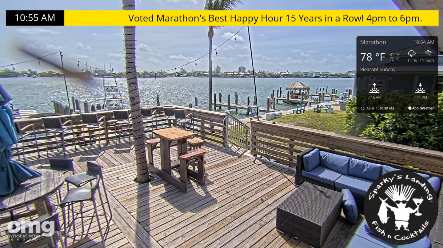 Wooden deck overlooking a sunny waterfront with tables and seating.
