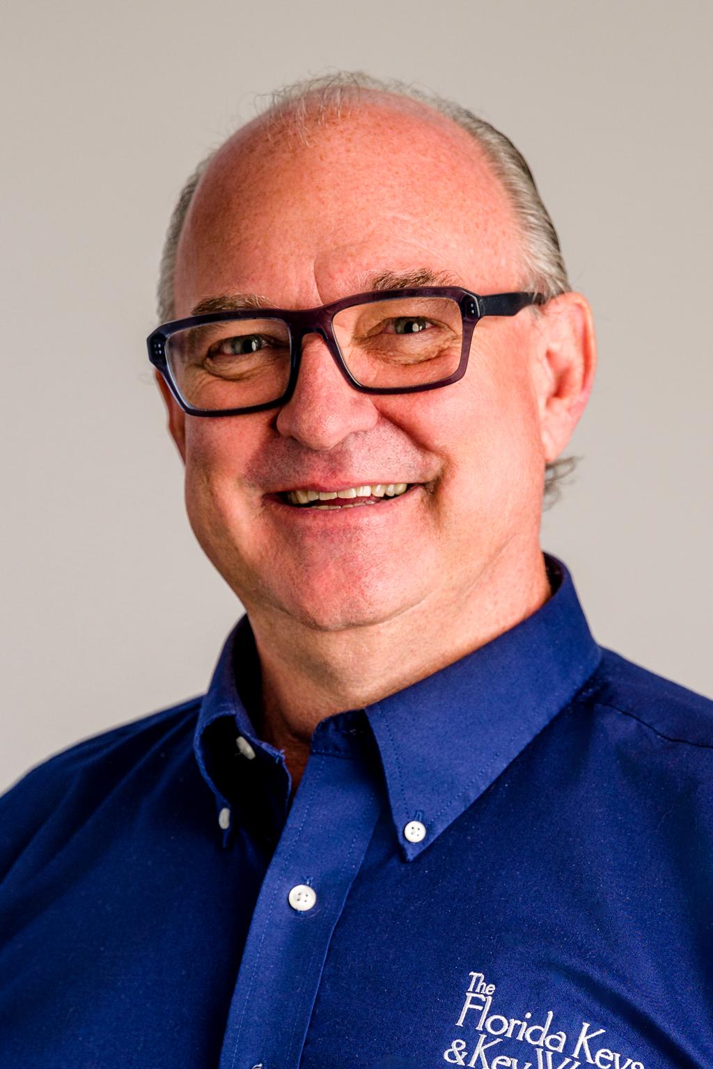 Smiling man wearing glasses and a blue shirt with embroidery.