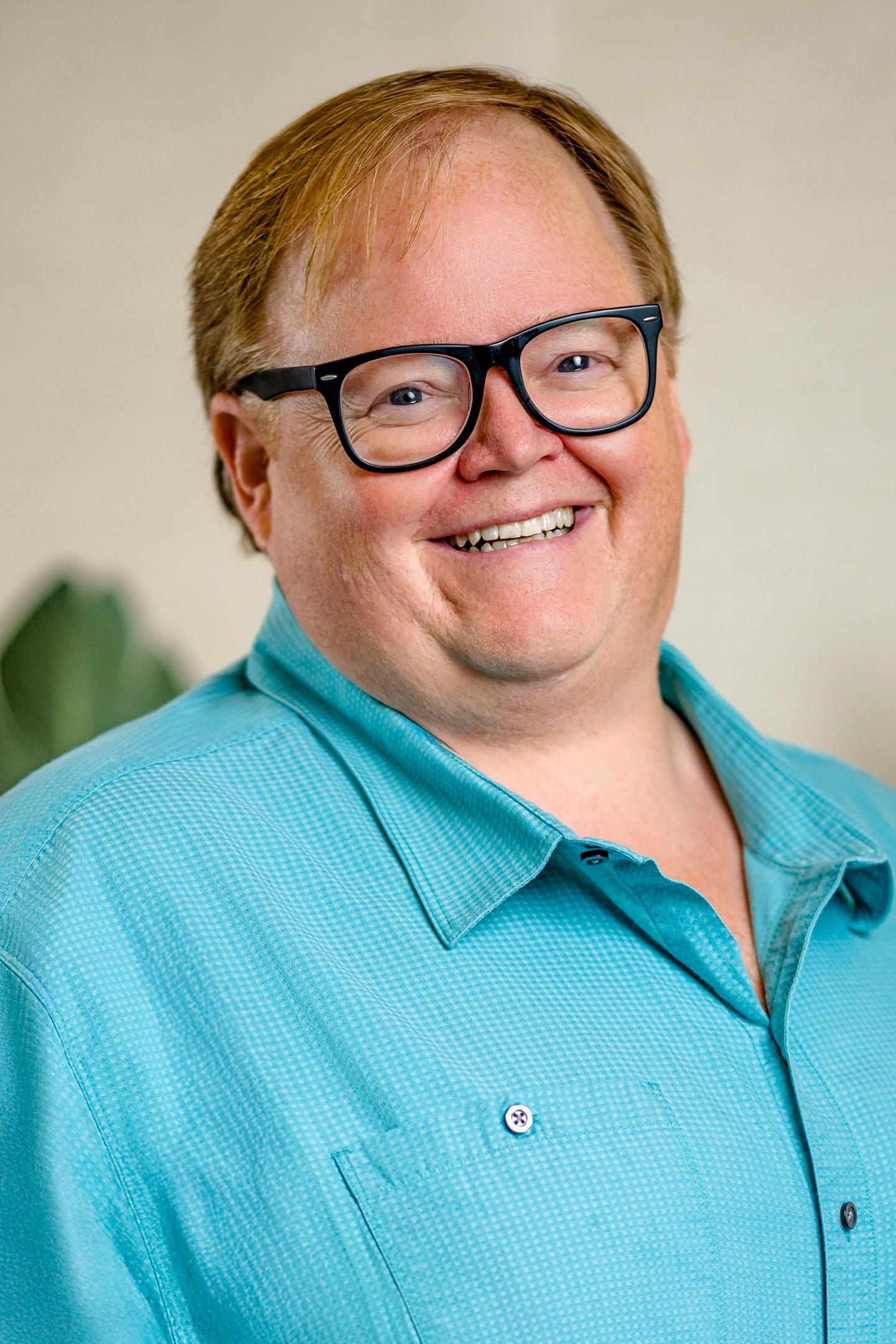 Smiling person with glasses and a blue shirt, indoors.