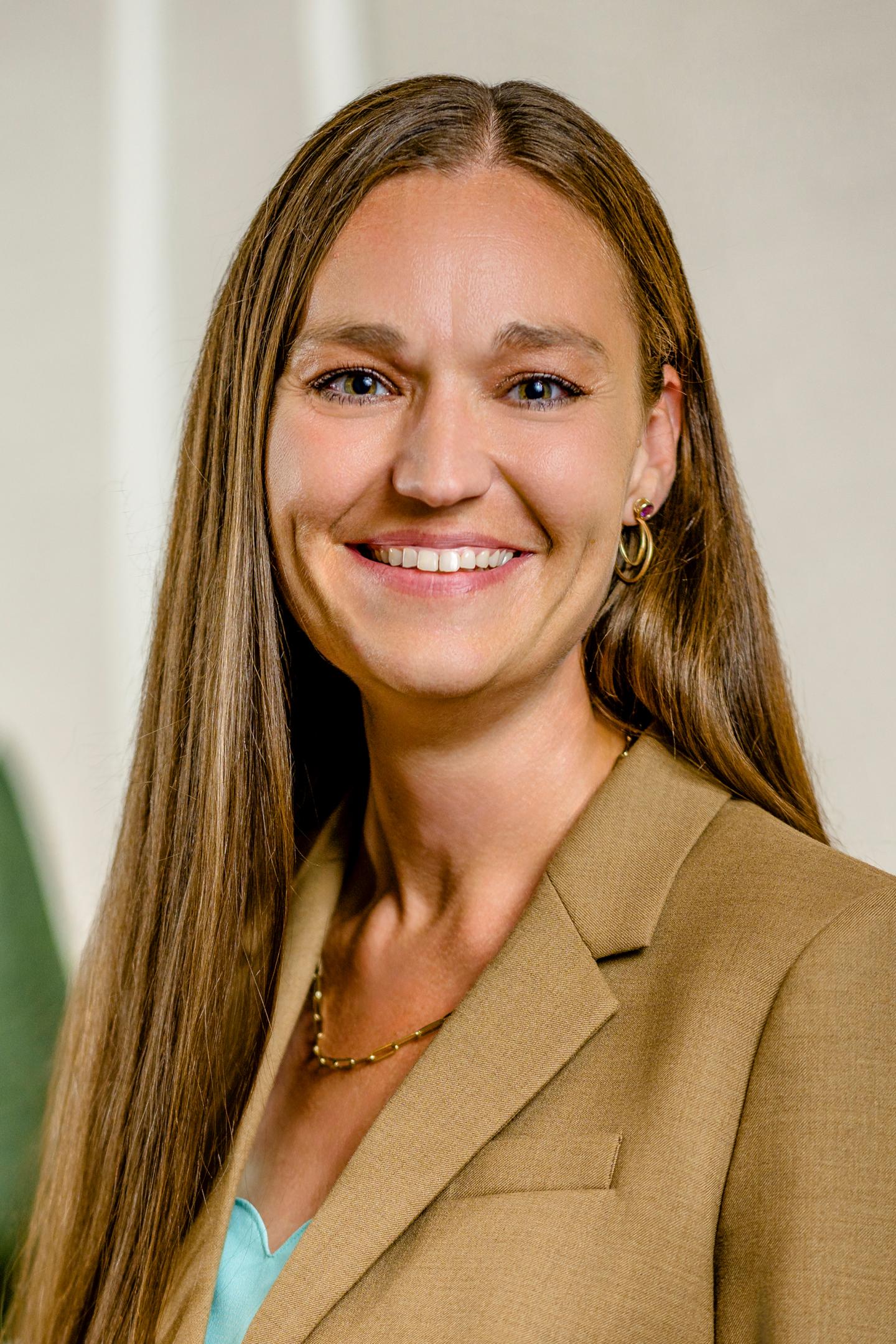 Smiling woman in a tan blazer with long brown hair.