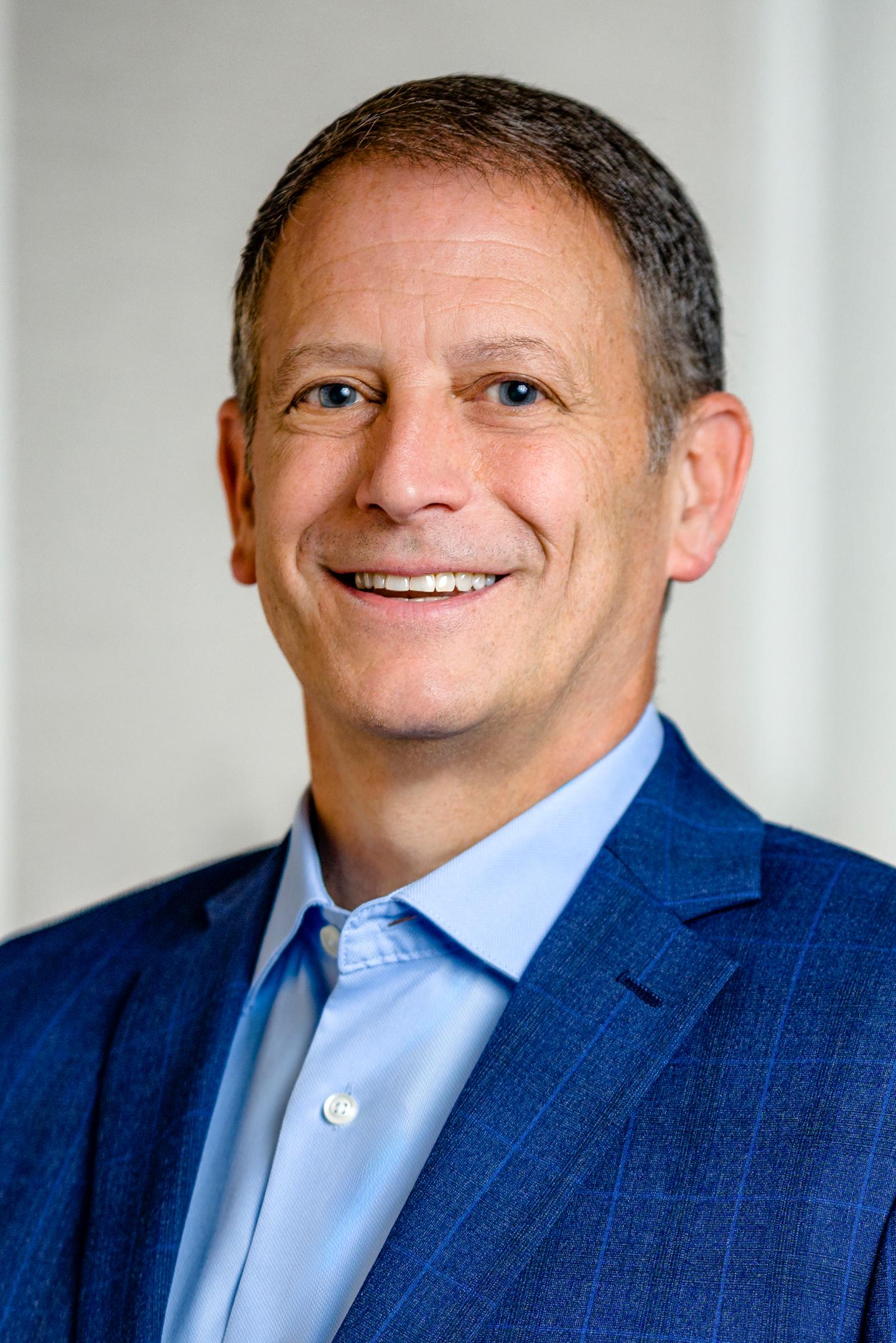 Smiling man in a blue suit and light blue shirt.