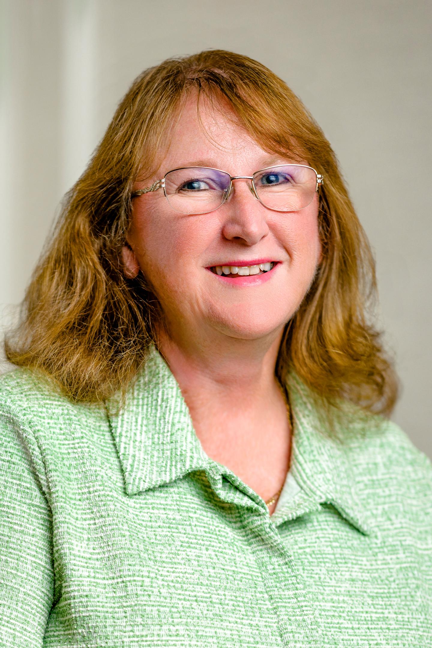 Smiling woman with glasses in a light green jacket.