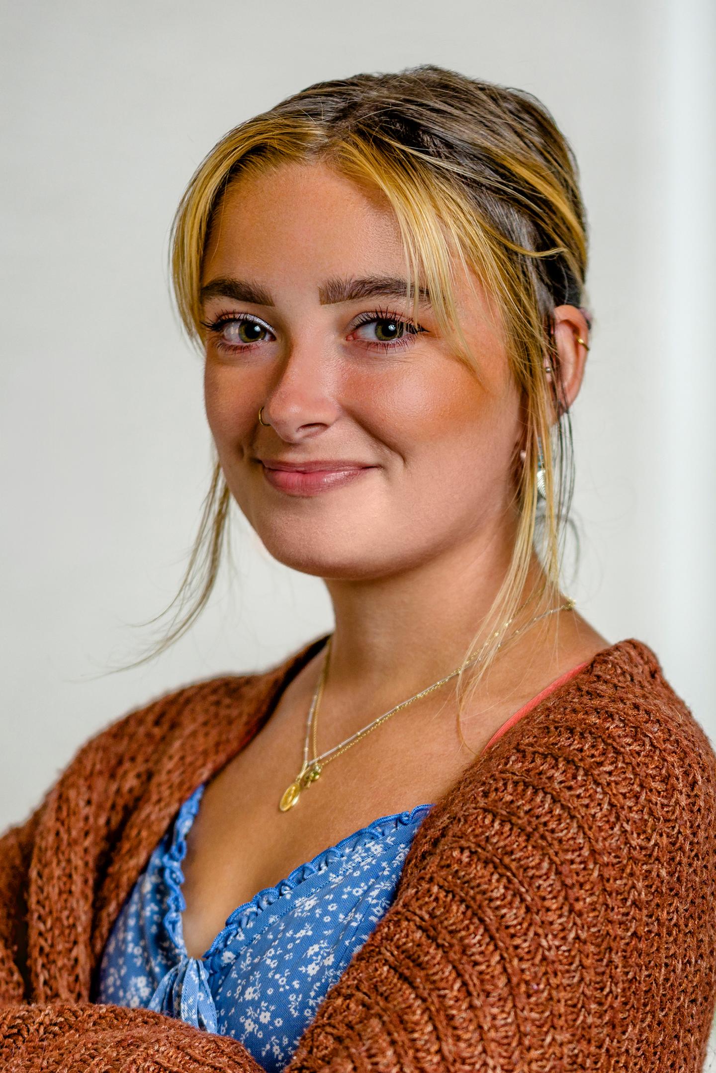 Smiling person in a blue top with a brown sweater, light background.