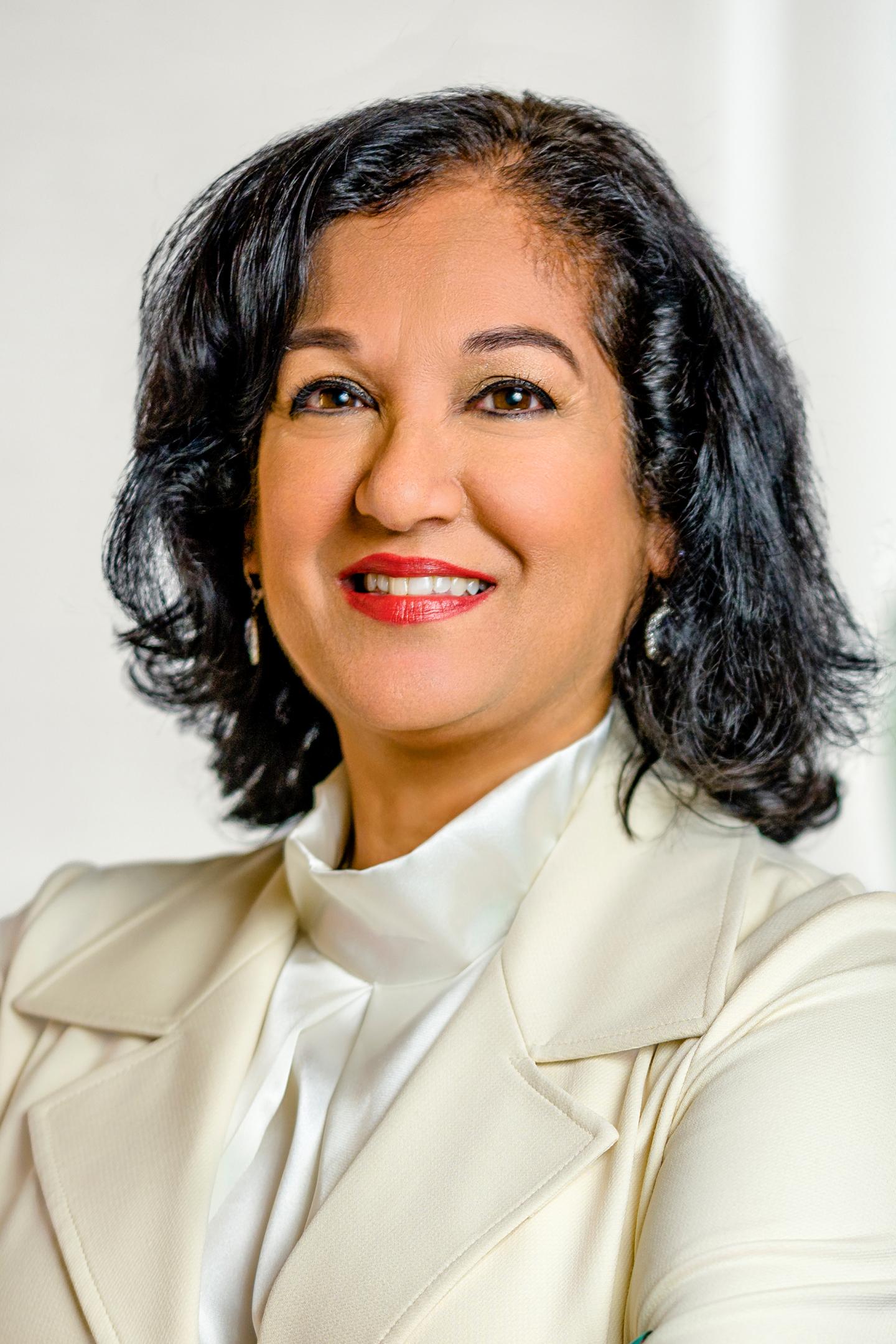 Smiling woman in a white blazer, photographed on a light background.