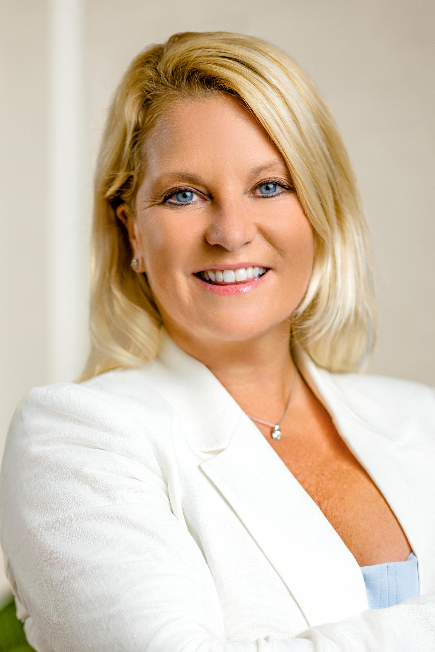 Blonde woman smiling in a white blazer.