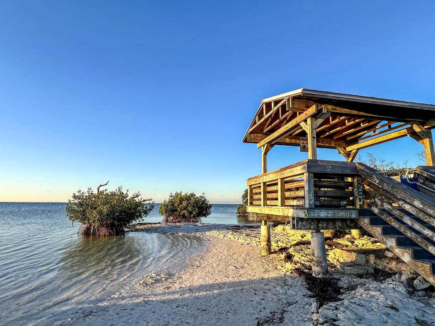 Beach with wooden gazebo, calm sea, and clear blue sky.