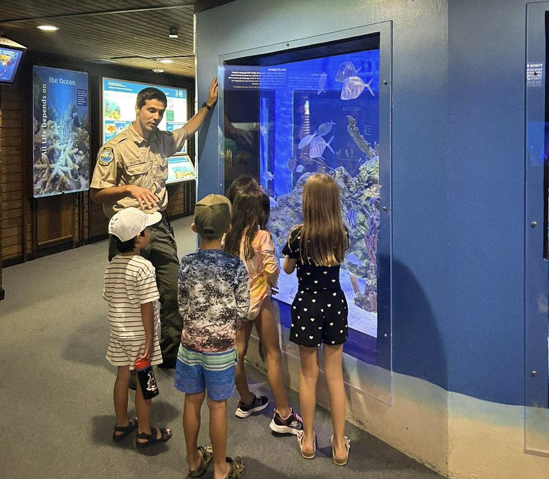 Children and a guide observe fish in a large aquarium display.