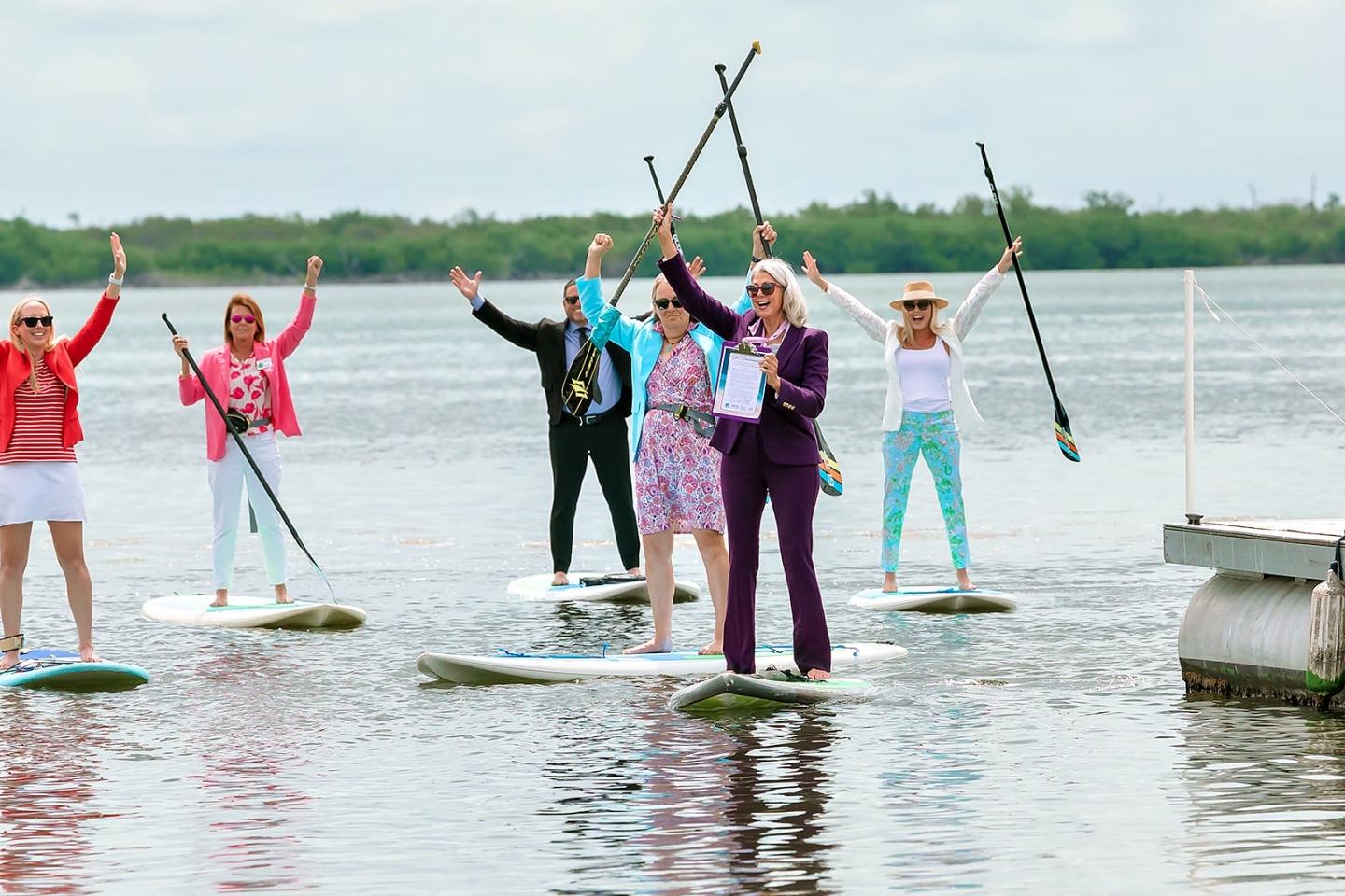 People stand on paddleboards, holding paddles above their heads on a calm lake.