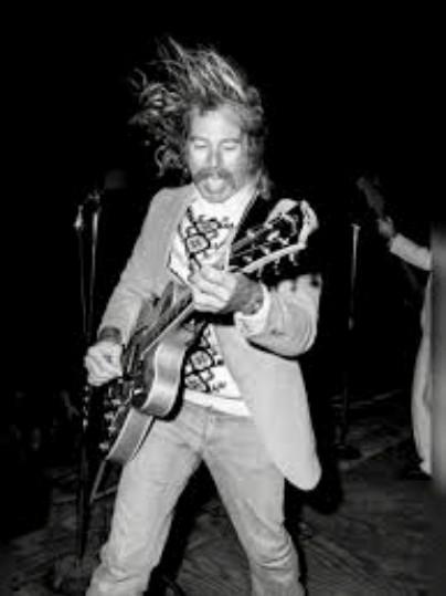 Musician energetically playing guitar with hair flying, on stage in black and white.