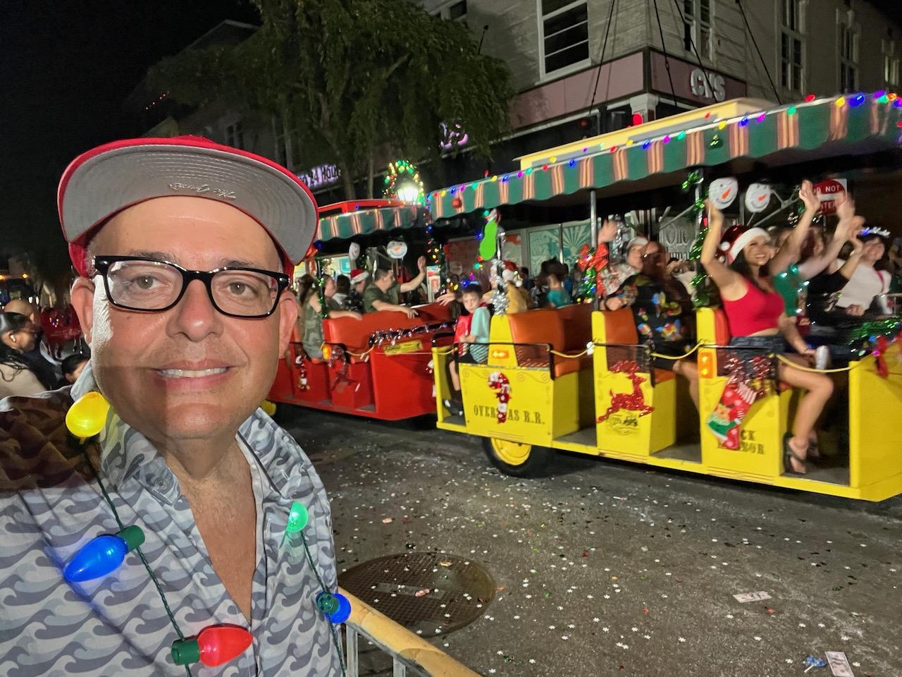 Man in festive shirt and hat at a colorful street parade at night.