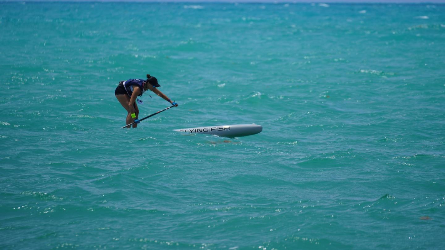 Paddleboarder kneeling on a board in turquoise ocean.
