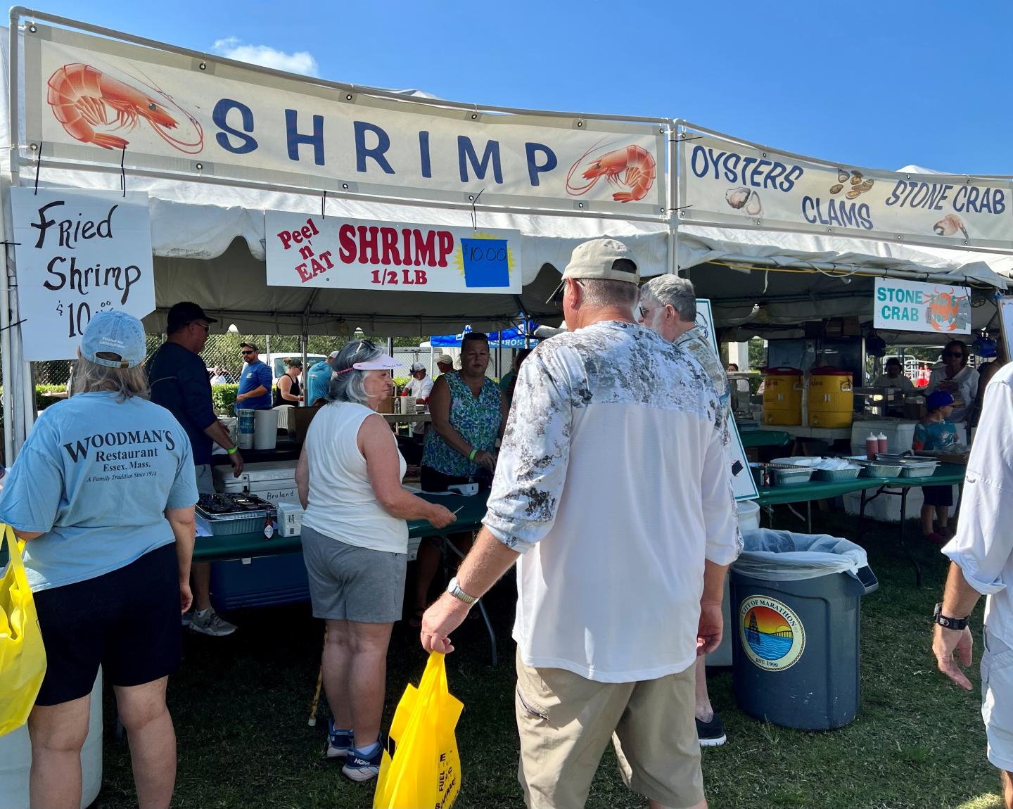 Shrimp festival booth with attendees under a blue sky.