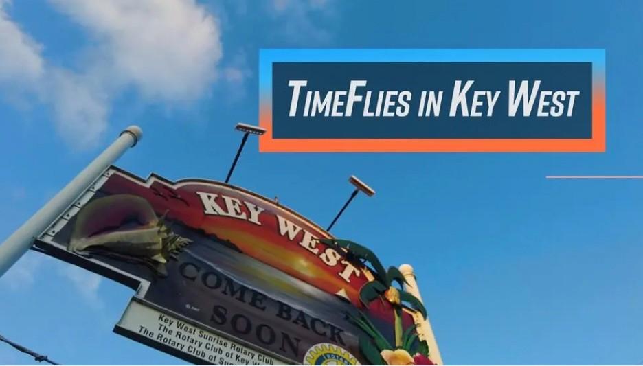 Key West sign under a blue sky, with colorful flowers attached.