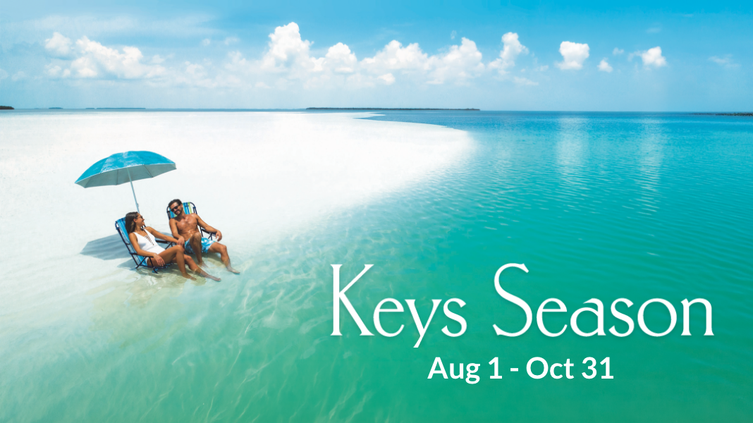 White sand beach with couple under blue umbrella by turquoise sea.