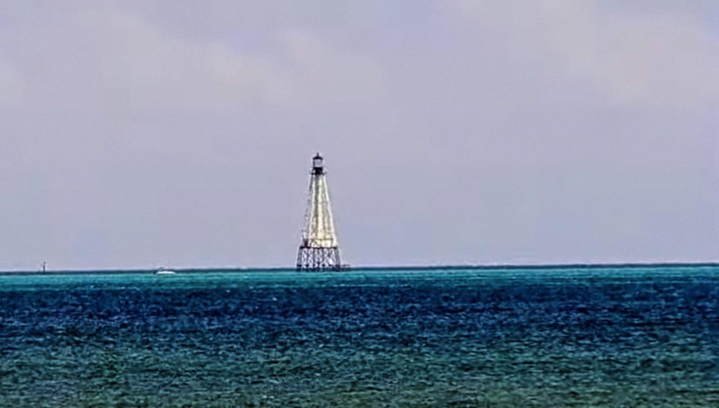 Lone lighthouse on calm blue sea under cloudy sky.