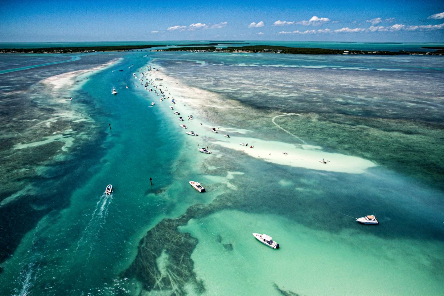 Aerial view of boats on turquoise water with a sandbar.