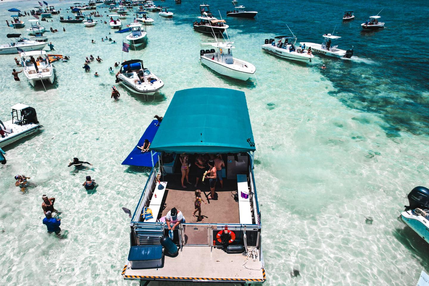 Boats anchored in clear, shallow water, people swimming and relaxing.