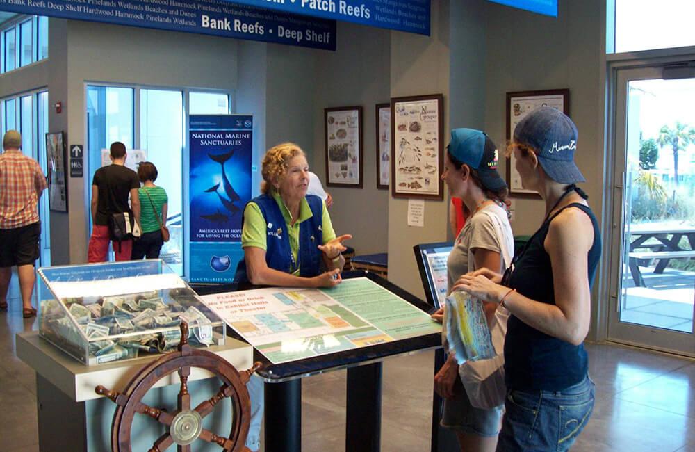 Visitor center with people talking by informational displays and a staff member providing assistance.