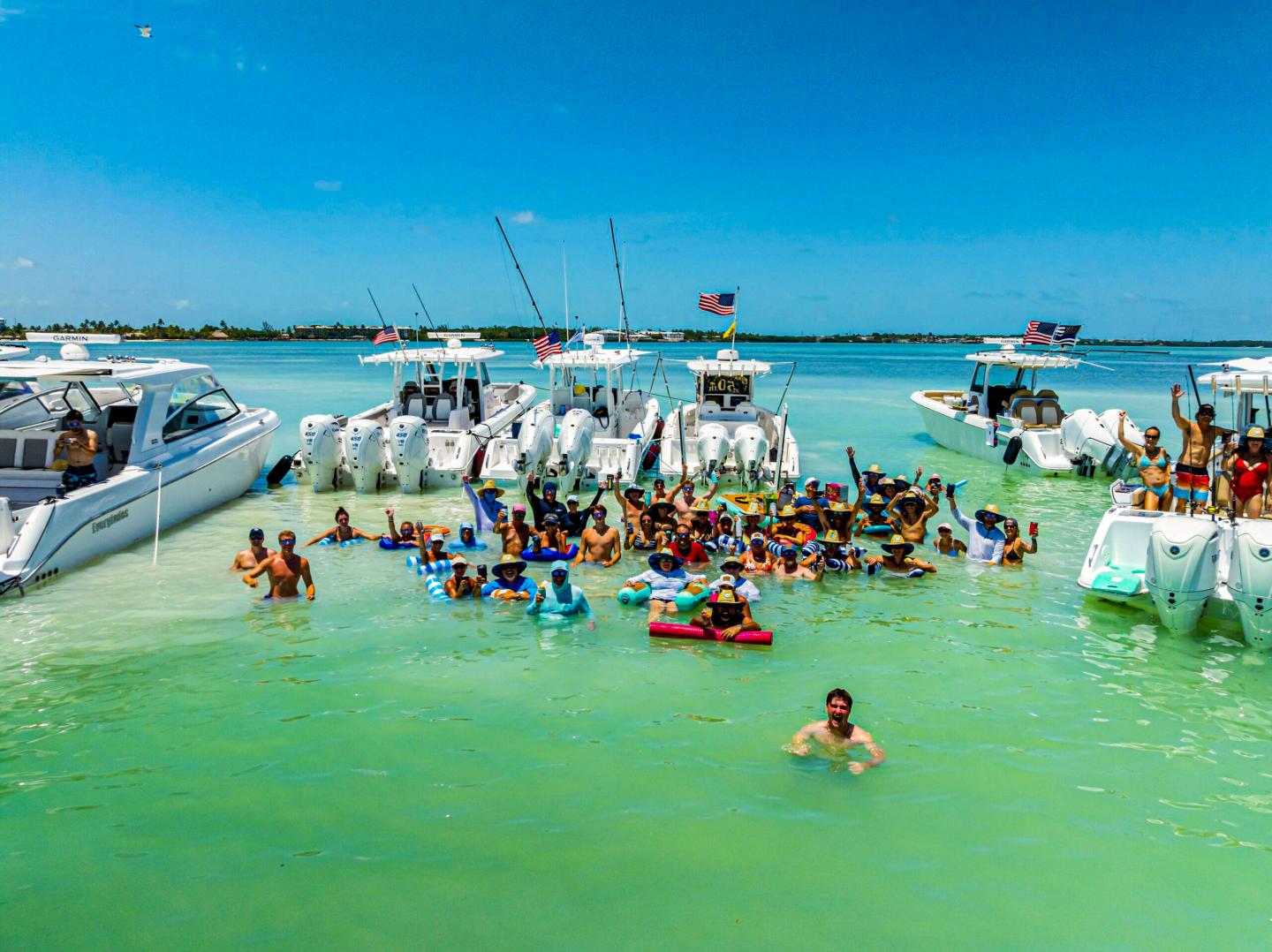 Boats anchored in turquoise water with people swimming and socializing.
